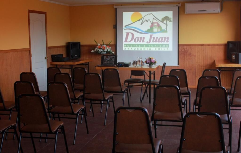Un salón de conferencias con filas de sillas, un atril y una pantalla de proyección que muestra “Don Juan Hostal & Turismo Araucania - Chile”.