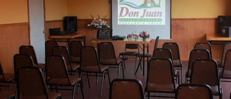 Un salón de conferencias con filas de sillas, un atril y una pantalla de proyección que muestra “Don Juan Hostal & Turismo Araucania - Chile”.
