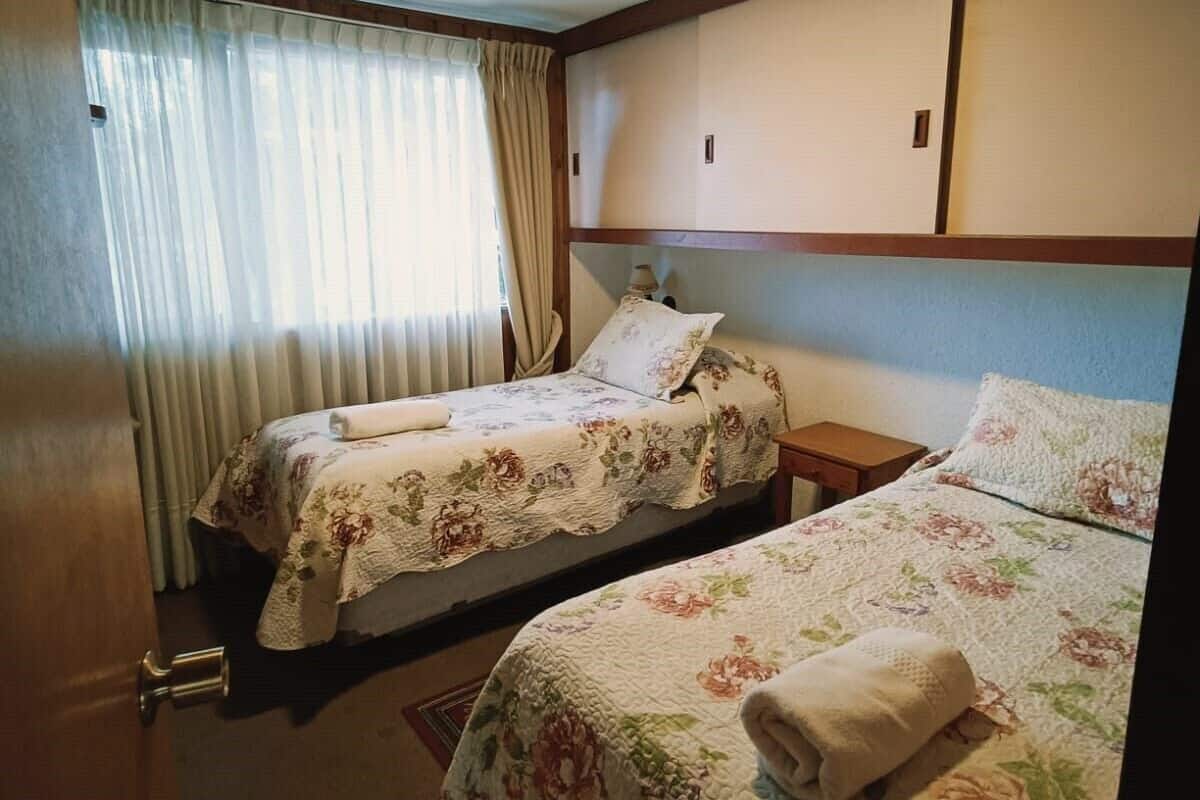Een hotelkamer met twee bedden, elk voorzien van bloemenprint beddengoed, een houten hoofdeinde en een plafondlamp.