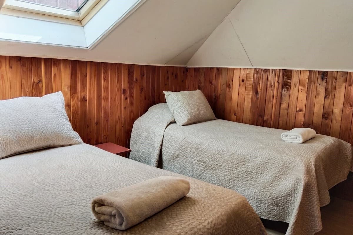 Een kamer met twee bedden, houten paneelwanden, een dakraam en een opgerolde handdoek op de vloer.