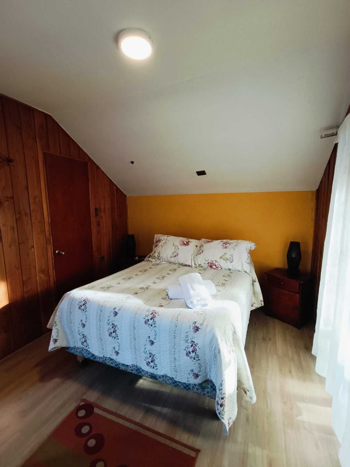 Un dormitorio con puerta de madera, cama con ropa de cama floral, una mesita de noche y una alfombra roja.