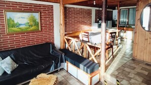 A rustic cabin interior with a black sofa, wooden dining table, and a painting on the brick wall. - Hostal & Cabañas Don Juan (Villarrica)