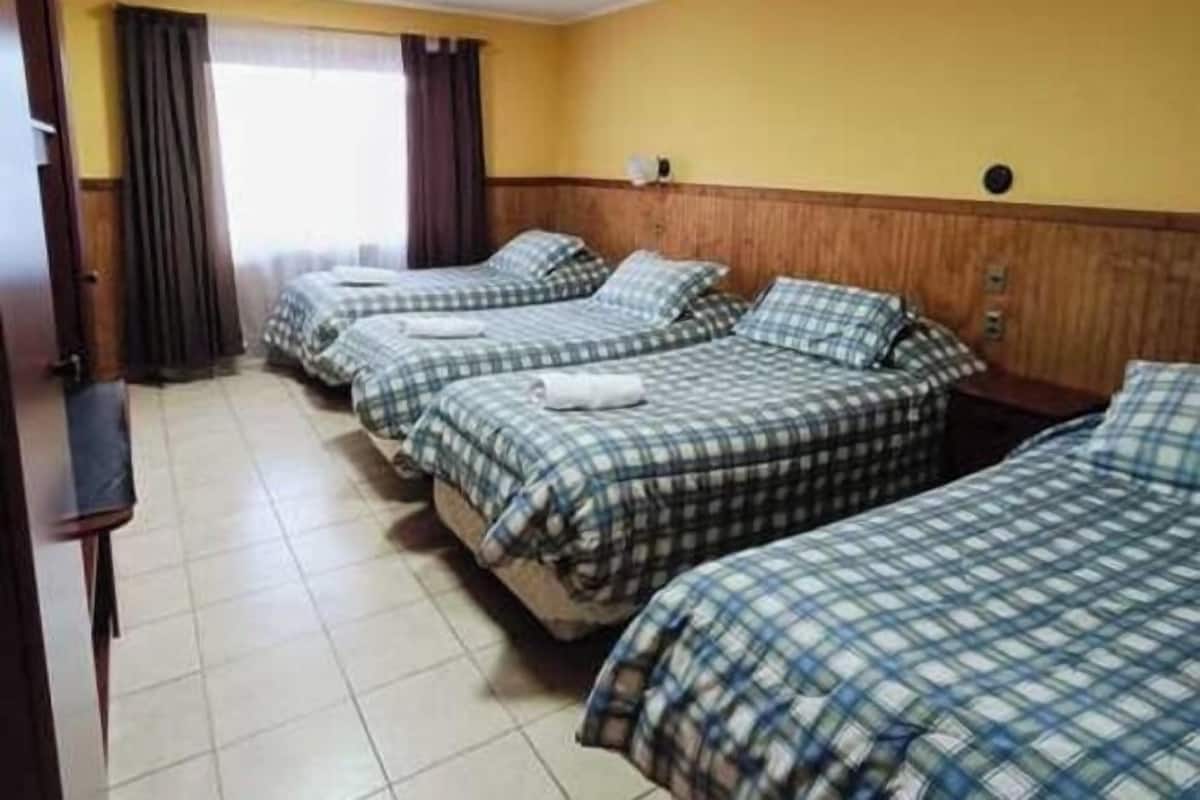 Een hotelkamer met drie bedden, elk voorzien van een geruit sprei, een houten hoofdeinde en een raam met gordijnen.