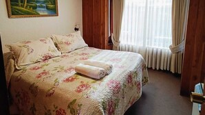 A hotel room with a bed, a painting, a window with curtains, and a door. - Hostal & Cabañas Don Juan (Villarrica)