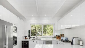 A modern kitchen with white cabinetry, a built-in oven, a stainless steel refrigerator, and a large window providing a view of greenery outside.