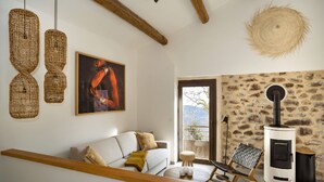 A cozy living room with a white sofa, a painting, wicker lamps, a stone wall, and a wood-burning stove.