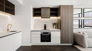 Une cuisine moderne avec des meubles blancs, un four encastré et un mur d’accent en bois.