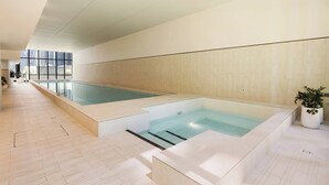 Une piscine intérieure moderne avec un plancher et des murs en bois, de grandes fenêtres et une plante en pot.