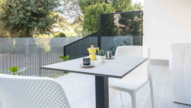 Eine moderne Terrassengruppe im Freien mit Tisch, Stühlen, einer Kaffeemaschine und einem Blumentopf.