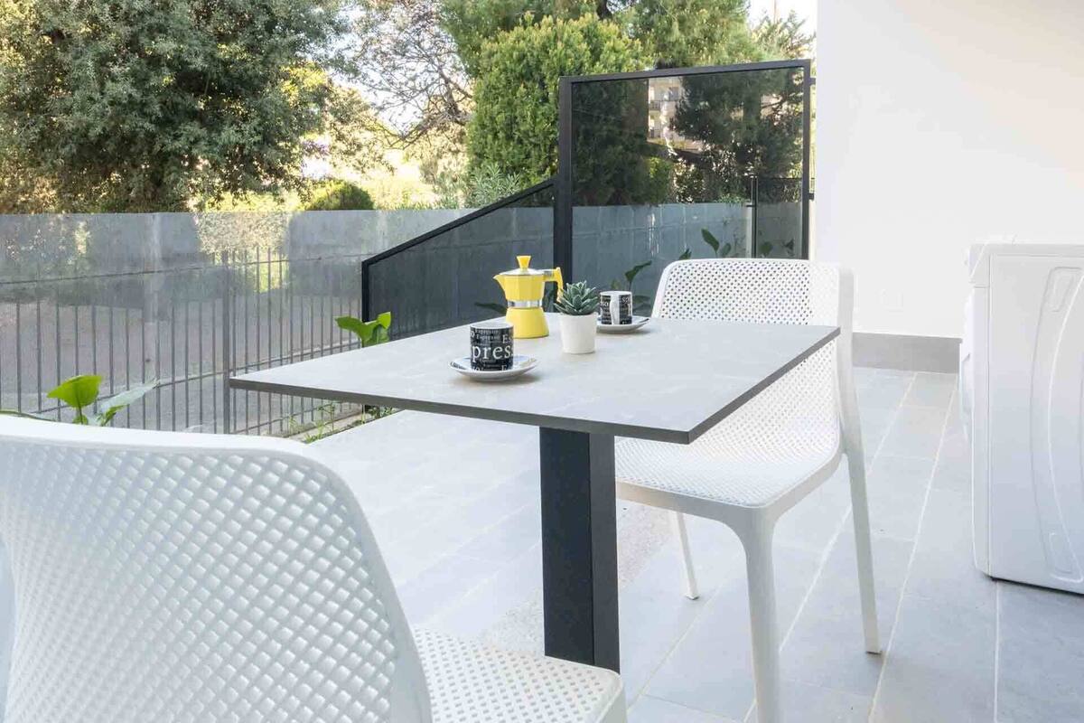 A modern outdoor patio with a table and chairs, a coffee maker, and a potted plant.
