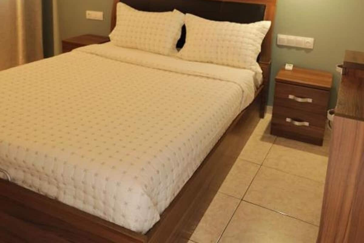 Una cama bien hecha con cabecera de madera, una mesita de noche con cajones y una lámpara colgante.