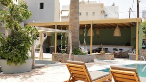 A poolside area with lounge chairs, a pergola, and a bar area. - Maria Apartments by Checkin (Hersonissos)