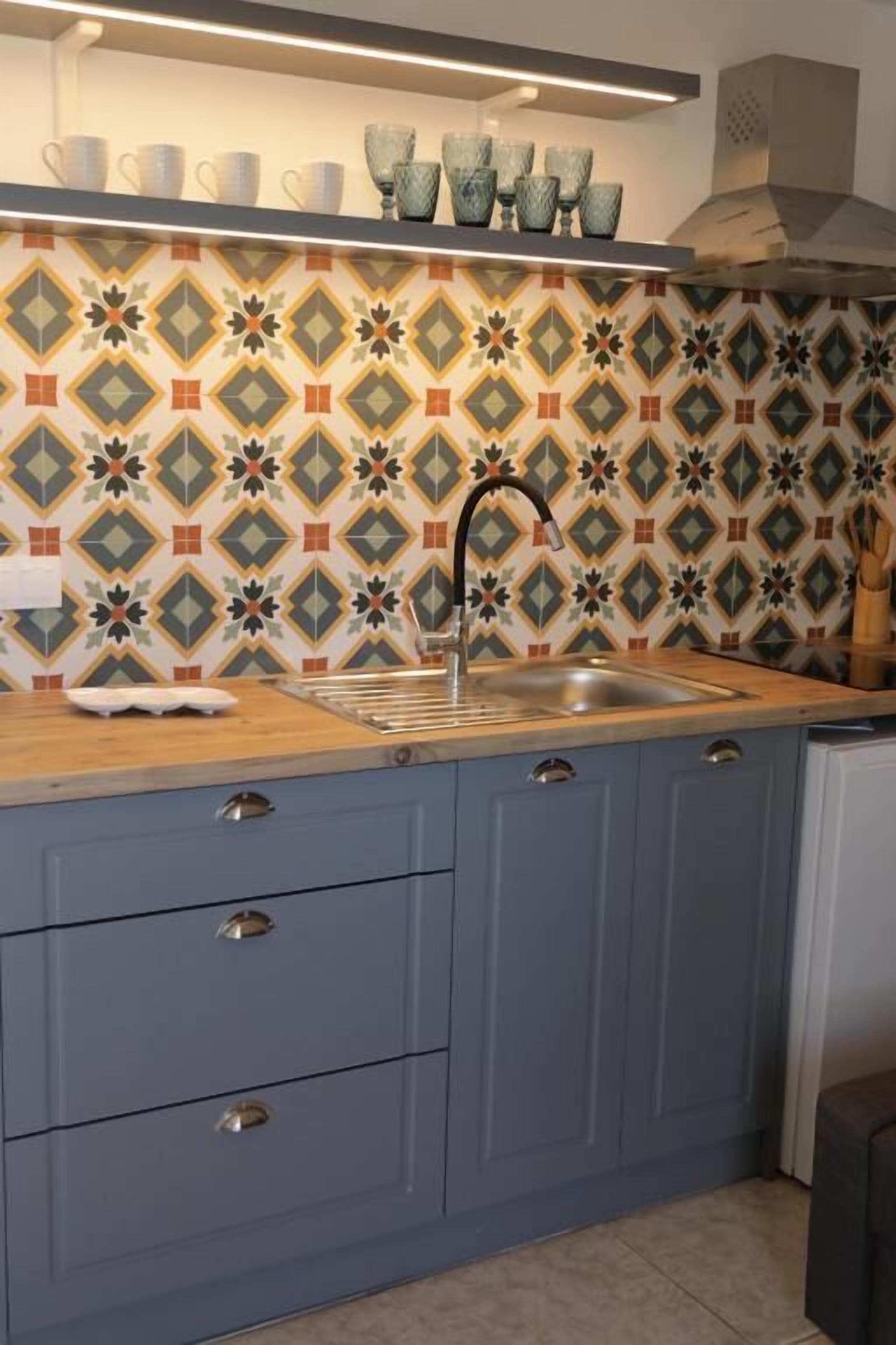A kitchen with a patterned backsplash, a sink, and blue cabinets.