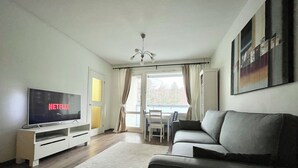 A modern living room with a flat-screen TV displaying 'NETFLIX', a grey sofa, a dining table with chairs, and a large window with curtains. - City Home Finland (Tampere)