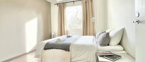A bedroom with a bed, bedside table, lamp, and window with curtains.