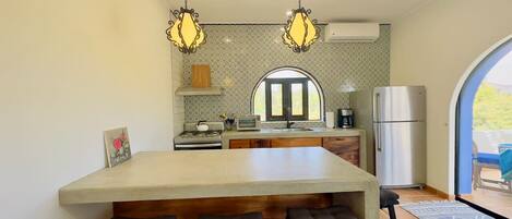A kitchen with a central island, bar stools, pendant lighting, a refrigerator, and a window with a view.