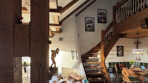 A rustic interior with exposed wooden beams, a staircase, and a dining area with wooden chairs and a table. - Exclusive maisonette apartment with alpine views (Ühlingen-Birkendorf)