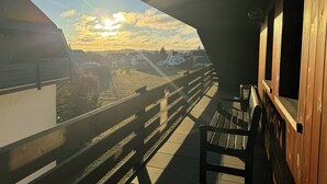 A balcony with a wooden railing overlooking a residential area during sunset. - Exclusive maisonette apartment with alpine views (Ühlingen-Birkendorf)