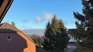 A residential street with a white car parked on the side, houses with red brick walls, and a clear blue sky. - Exclusive maisonette apartment with alpine views (Ühlingen-Birkendorf)