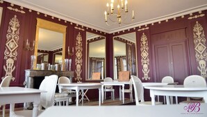 A dining area with white furniture, a chandelier, and ornate wall decorations. - Château de la Motte Beaumanoir (Pleugueneuc)