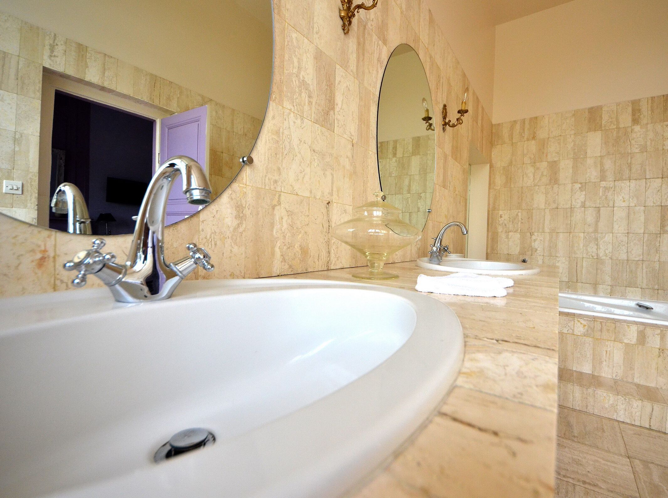 Un baño con un lavamanos ovalado grande, un espejo y un mueble tocador con un lavabo pequeño.