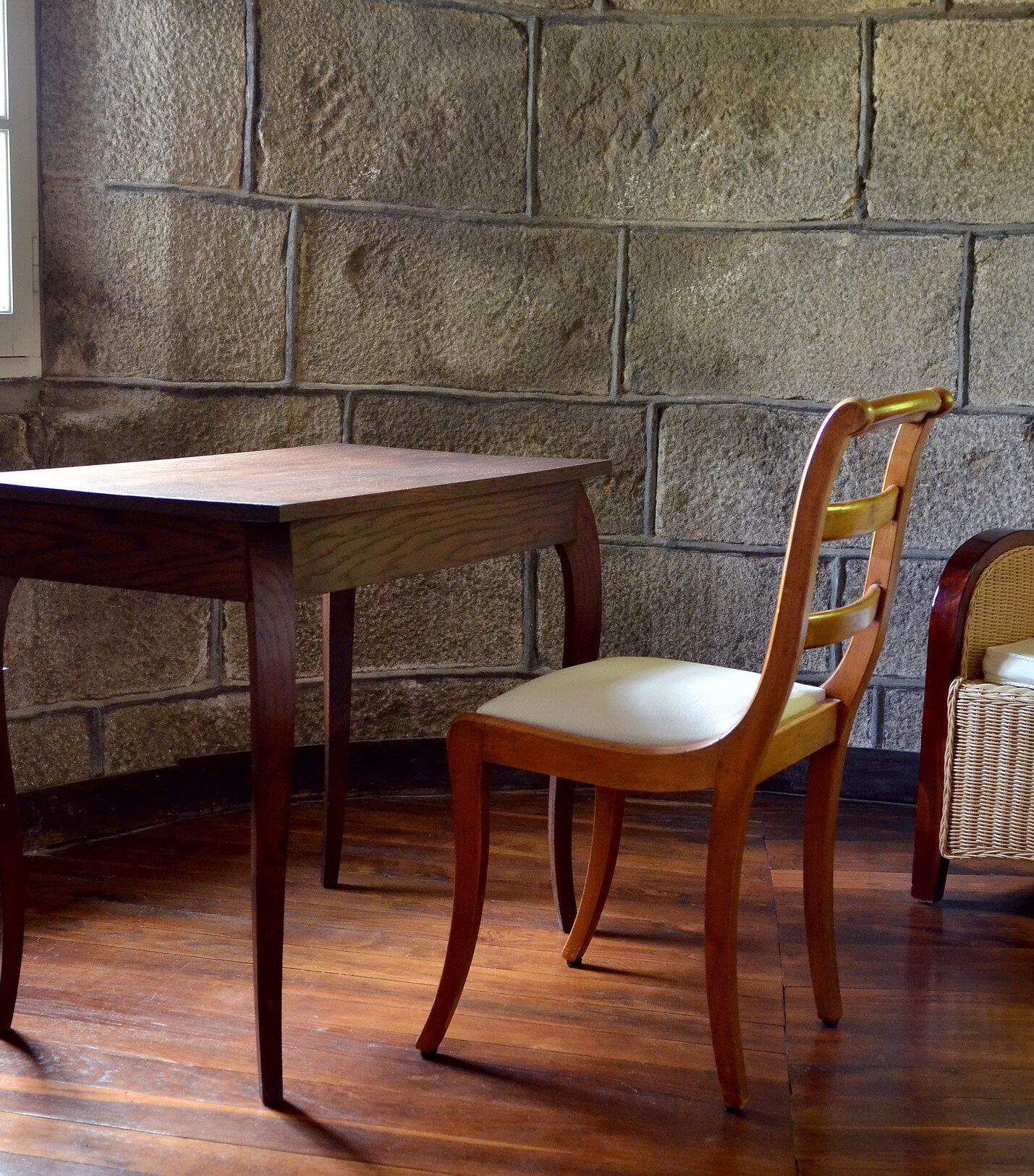 A wooden table and chair in a room with stone walls and wooden flooring.