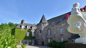 A historic stone building with a tower, ivy-covered walls, and a statue in the foreground. - Château de la Motte Beaumanoir (Pleugueneuc)