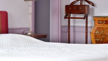 Un letto rifatto con un copriletto bianco, un piccolo comodino in legno con una lampada e una cassettiera in legno con cassetti.
