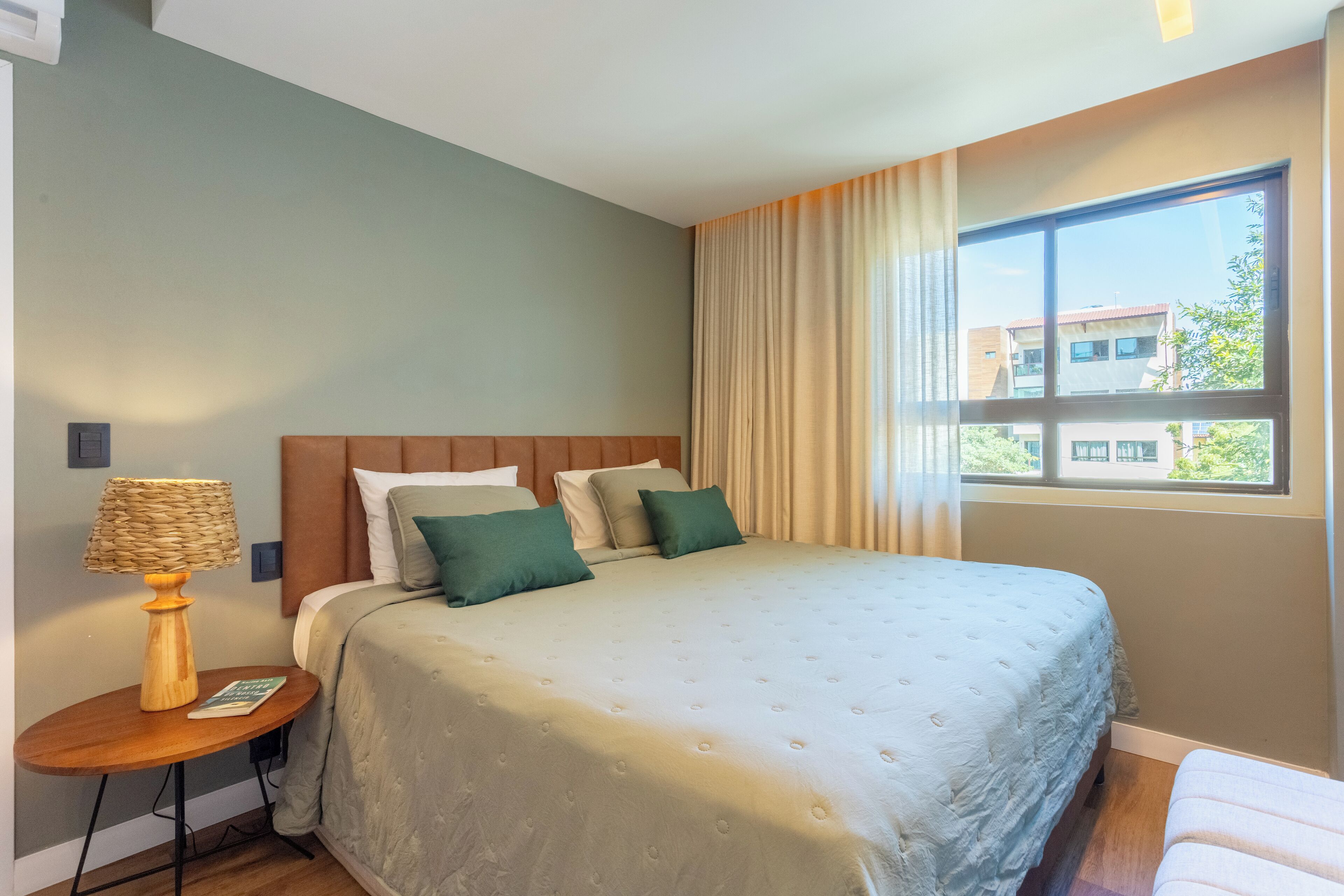 Ein Schlafzimmer mit einem großen Bett, einem Nachttisch mit Lampe und einem Fenster mit Vorhängen.