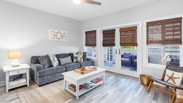 A modern living room with a grey sofa, white coffee table, and a ceiling fan. - Cassine Way 303 - Seagrove + Sunsets (Santa Rosa Beach)