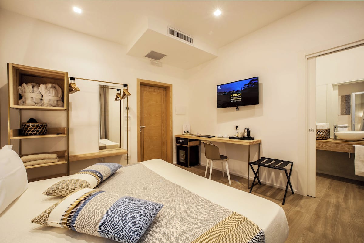A modern hotel room with a bed, a desk, a television, and a wardrobe.