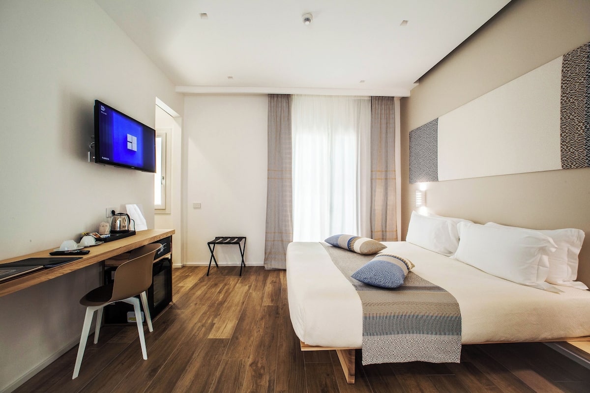 A modern hotel room with a bed, a desk, and a television.