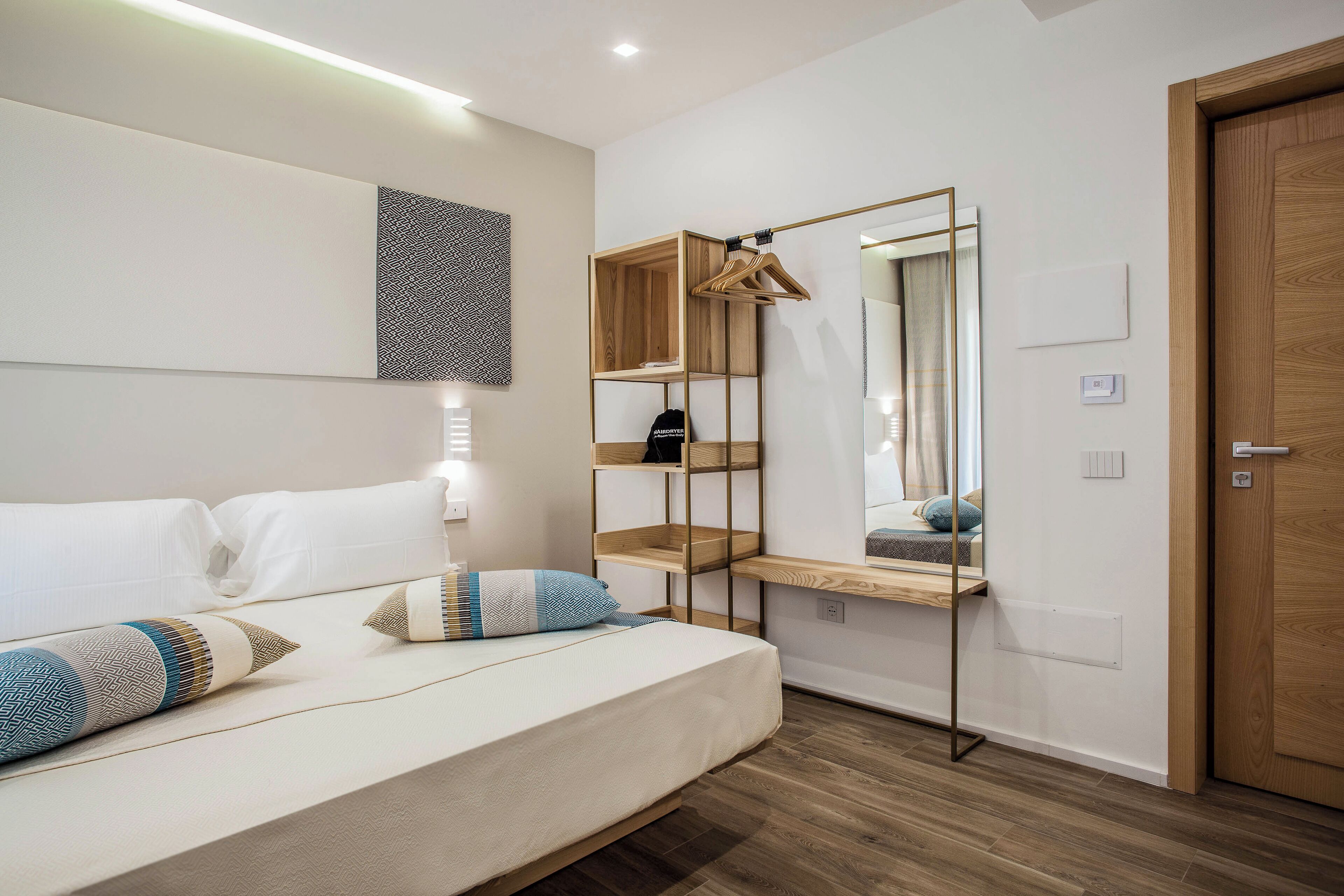 A modern bedroom with a bed, bedside tables, a mirror, and a wooden door.