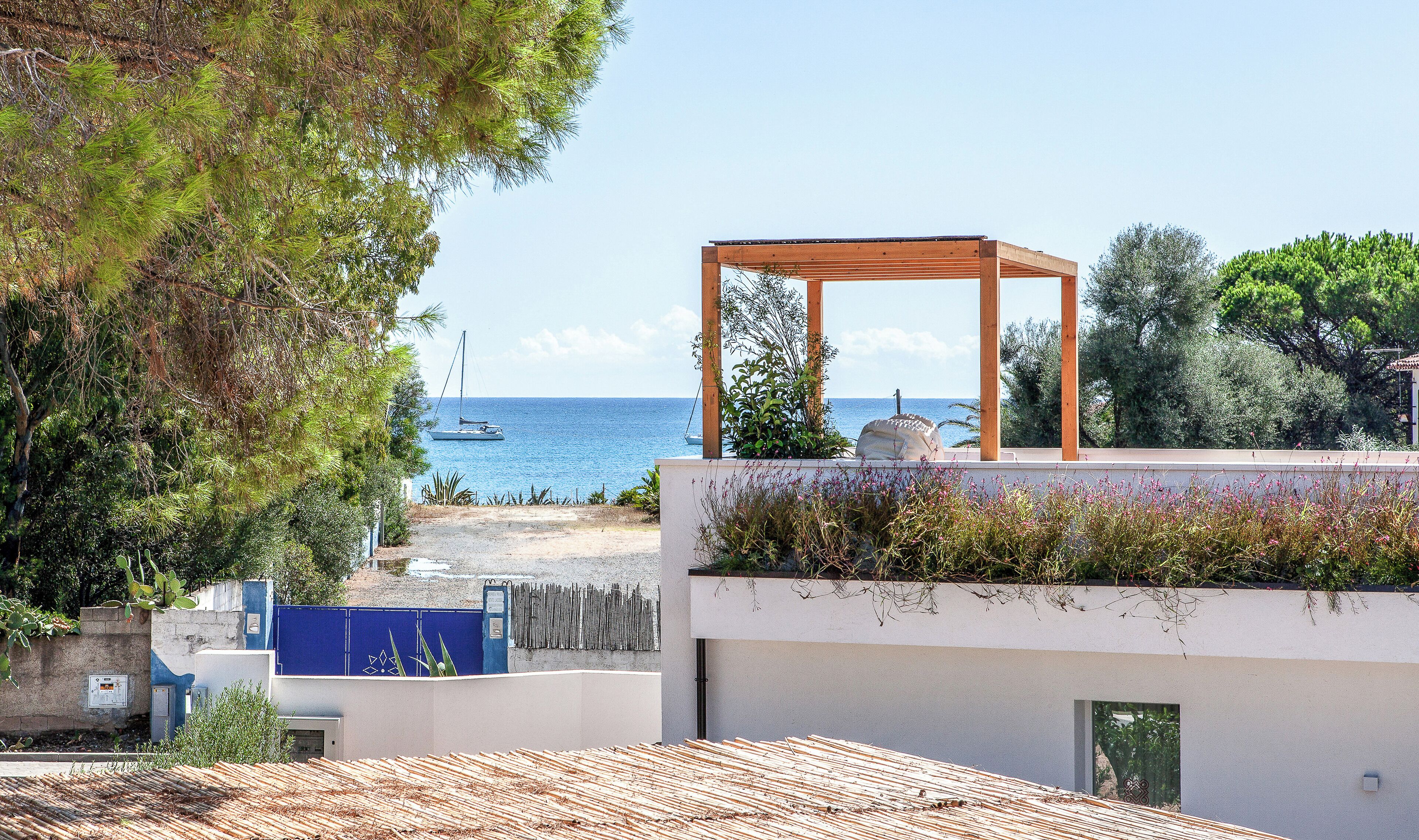 Eine Dachterrasse mit einer Pergola, Blick auf das Meer und ein Segelboot in der Ferne.