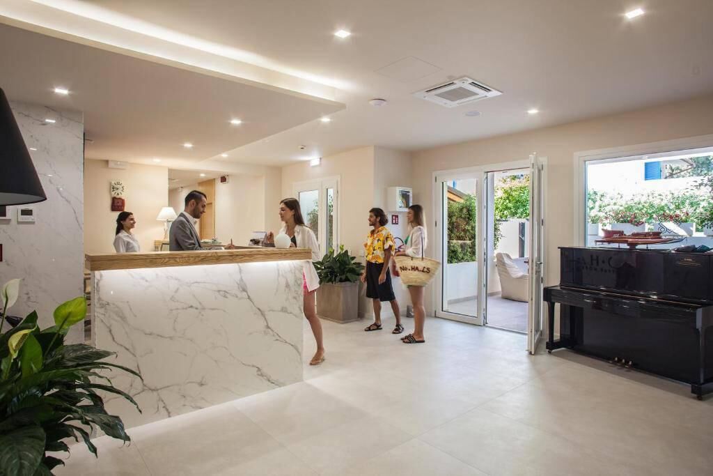 Zona de recepción de un hotel con mostrador de mármol, un piano y vistas al exterior.
