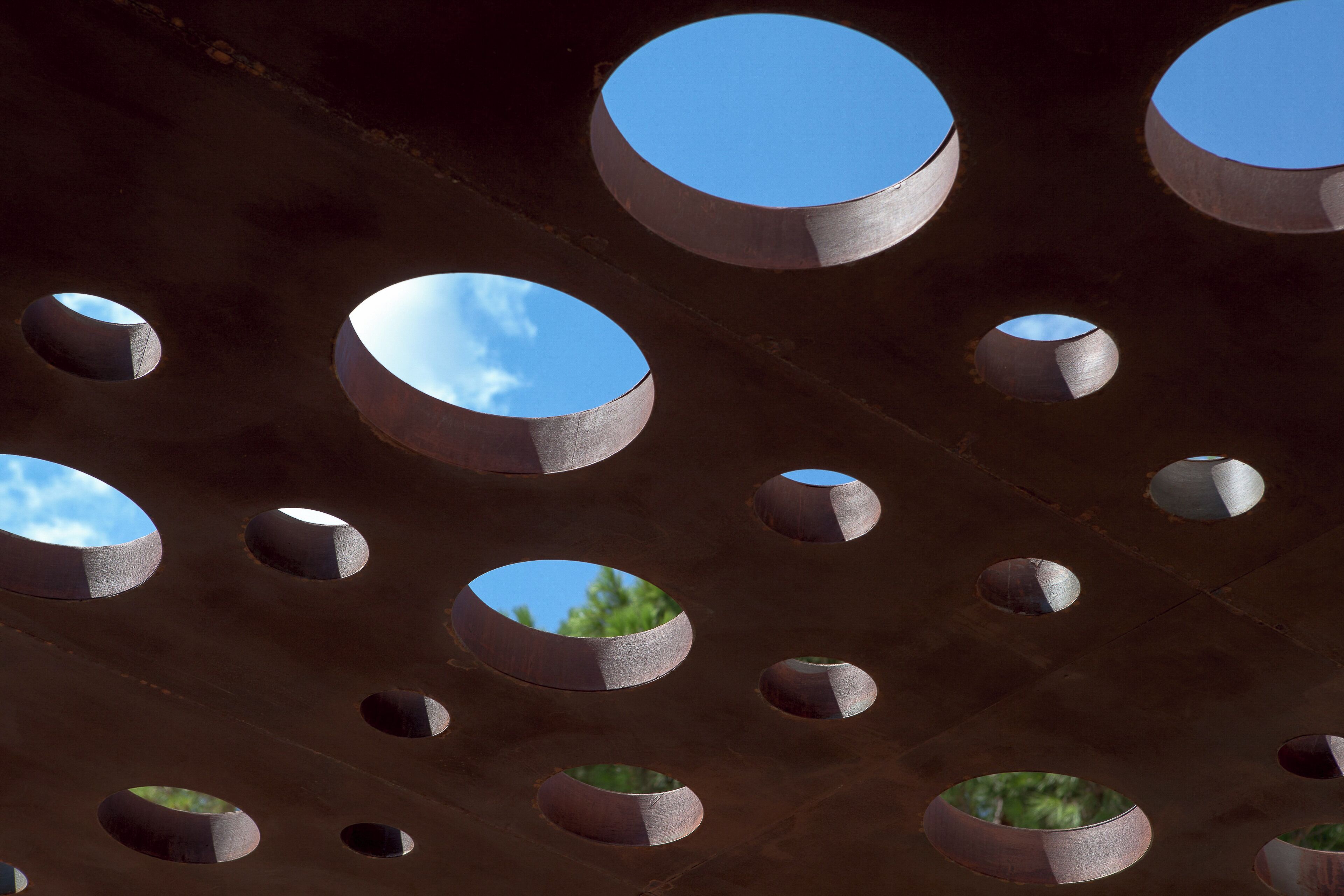 A ceiling with multiple circular openings, some with visible sky through them.