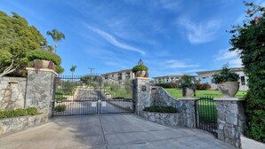 A gated entrance with a stone wall and a metal gate, leading to a building with a red roof and a garden. - Marvelous 11-bedroom villa in Escondido (Escondido)