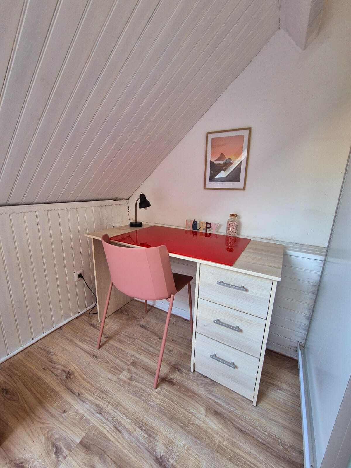 A small, sloped ceiling room with a desk, chair, and a framed picture on the wall.