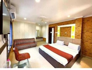 A hotel room with a large bed, a sofa, a chair, and a TV. - DhamStay Hotel Sai Sandpiper Near Beach (Puri)