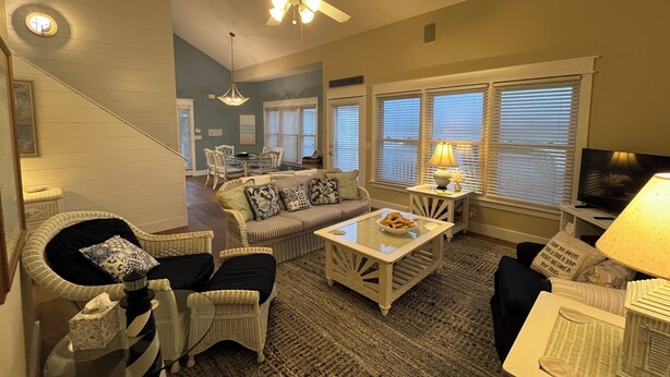 A living room with a sofa, chairs, a coffee table, a television, and a ceiling fan.