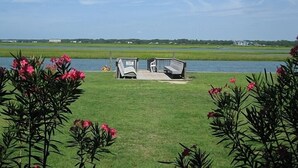 A grassy area with two benches facing a body of water, surrounded by flowering plants.