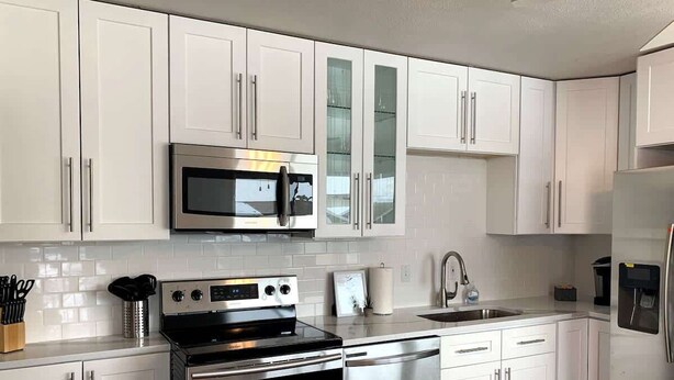 Uma cozinha moderna com armários brancos, eletrodomésticos de aço inoxidável e painel de azulejos.