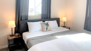 Quarto de hotel com uma cama grande, duas luminárias de cabeceira, uma janela com cortinas e vista para o exterior.