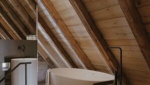 Et soveværelse på loftet med træloft, badekar og glasgelænder.