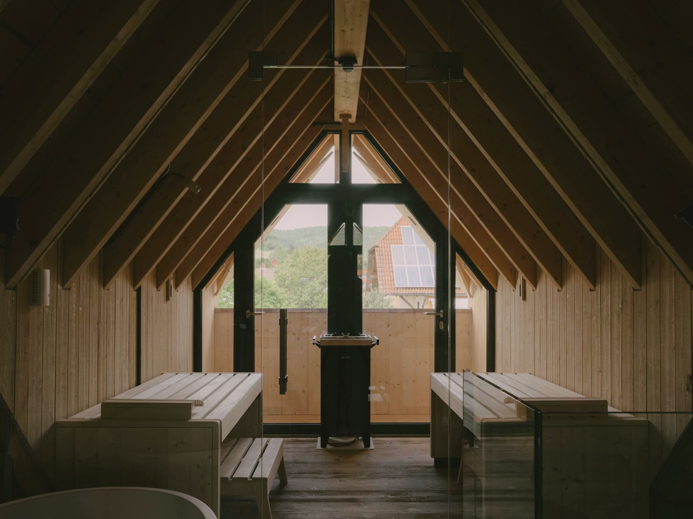 An attic room with wooden walls, a central chimney, and benches along the walls.