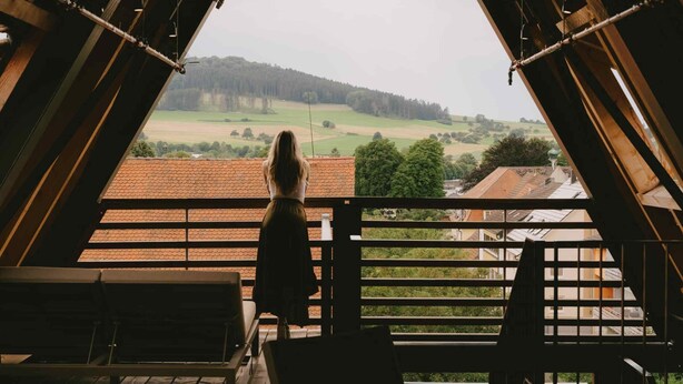 En kvinde står på en balkon med udsigt over et landligt landskab.
