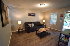 A living room with a dark leather sofa, two side tables with lamps, a coffee table, and a painting on the wall.