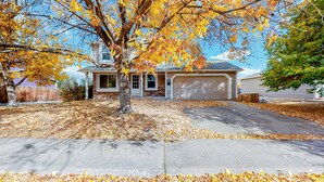 Une maison d’habitation avec un garage, une allée et un arbre aux feuilles d’automne.