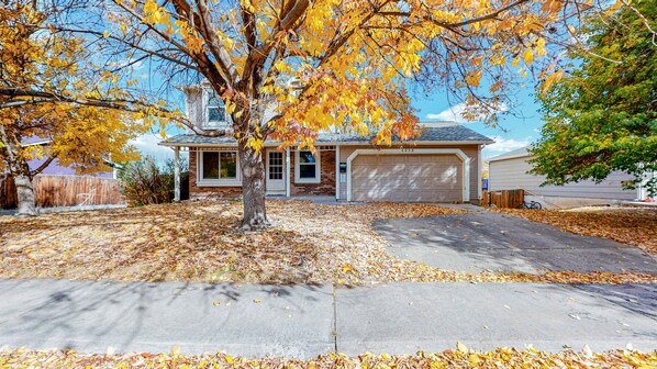 A residential house with a garage, driveway, and a tree with autumn leaves.
