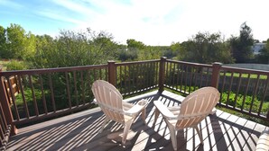 Una terraza de madera con dos sillas Adirondack orientadas a un exuberante paisaje verde.